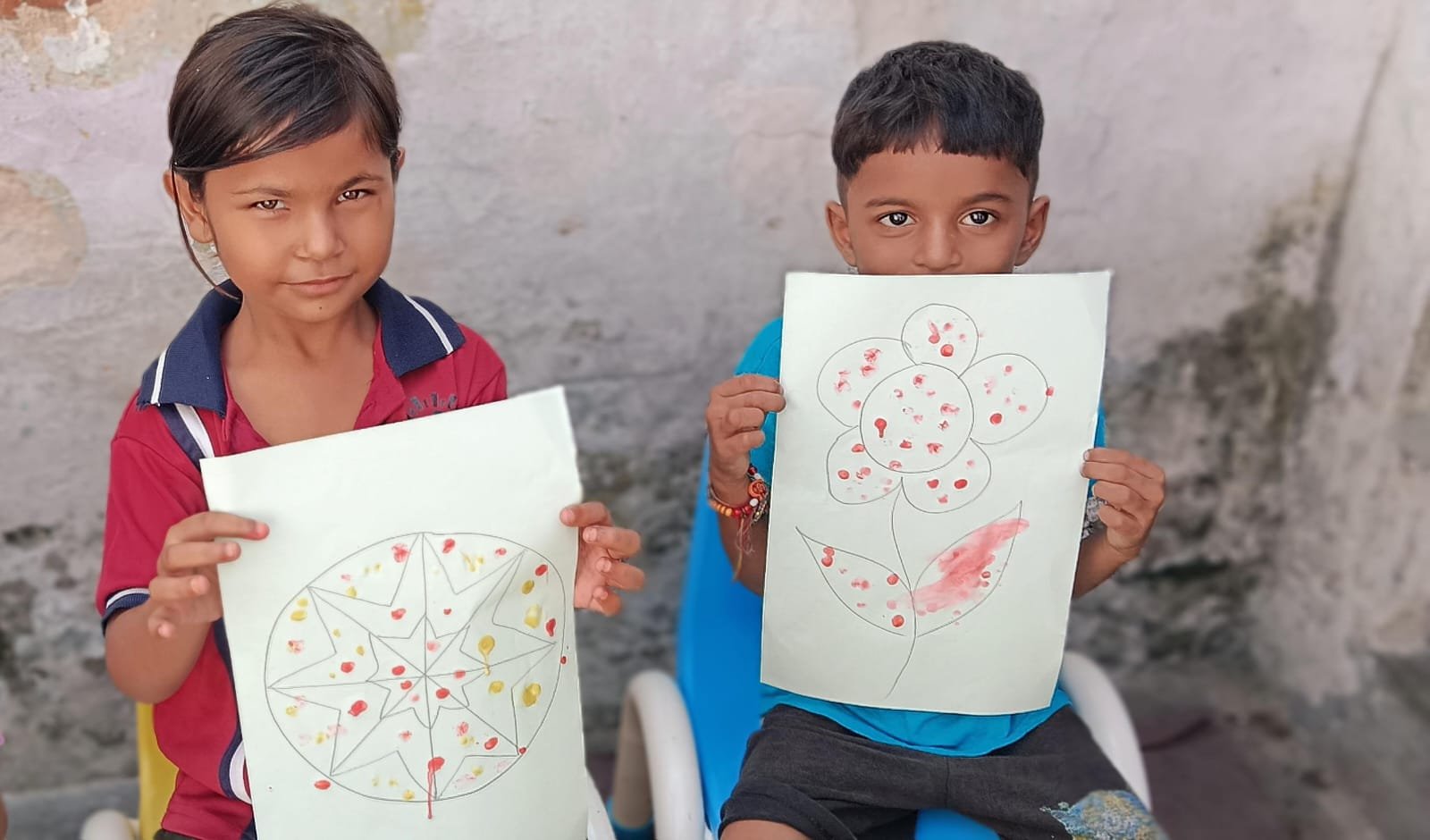 Two children proudly holding up their finger-painted drawings