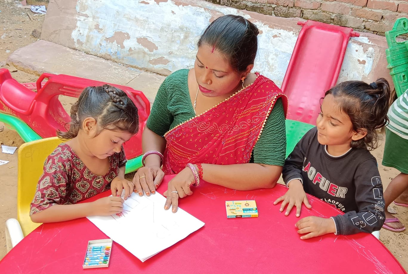 A Shiksha Ki Ore teacher helping two children with drawing